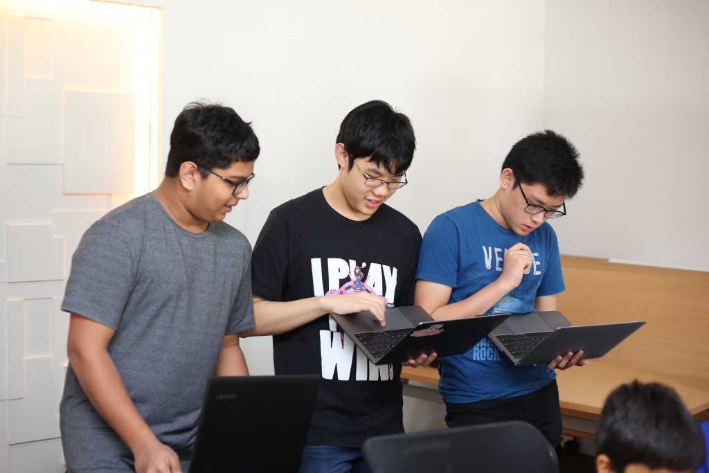 Three students discussing coding on laptops