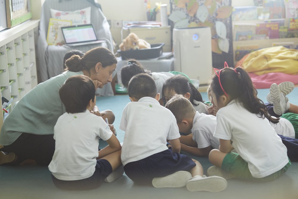 students reading with teacher on floor at school